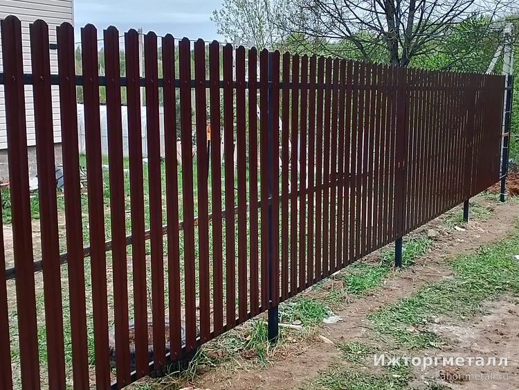 Длинный забор из коричневого металлического штакетника, столбы видны ниже планок